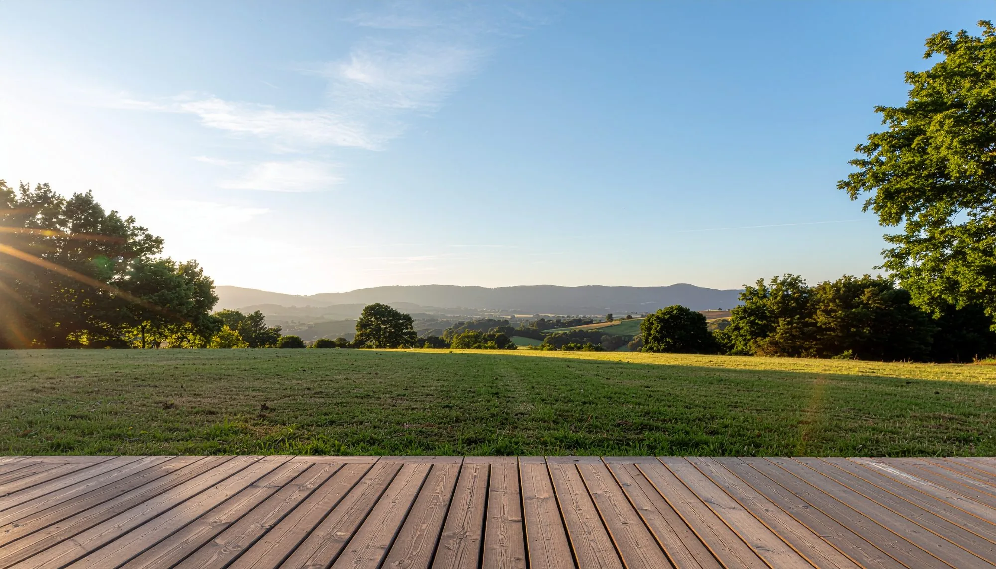Terrasse bois ouvrant sur la pelouse, collines au loin